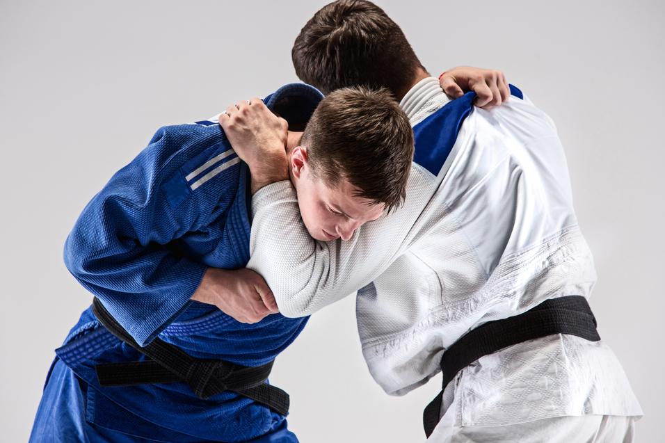 Zwei Judokas führen einen Wettkampf mit Griffen in blauer und weißer Judokleidung aus.
